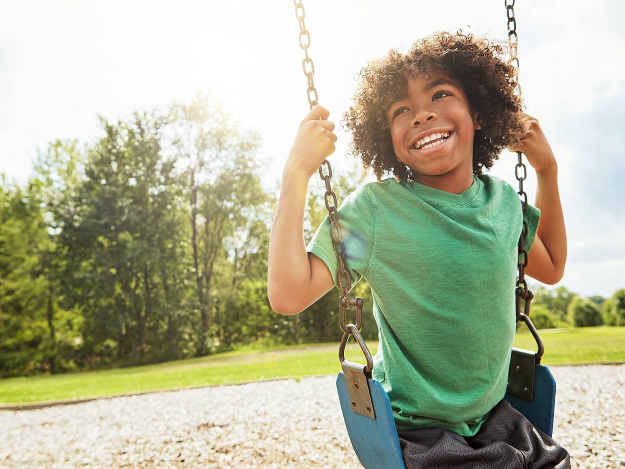 Smiling African American boy in a green t-shirt sitting on a swing