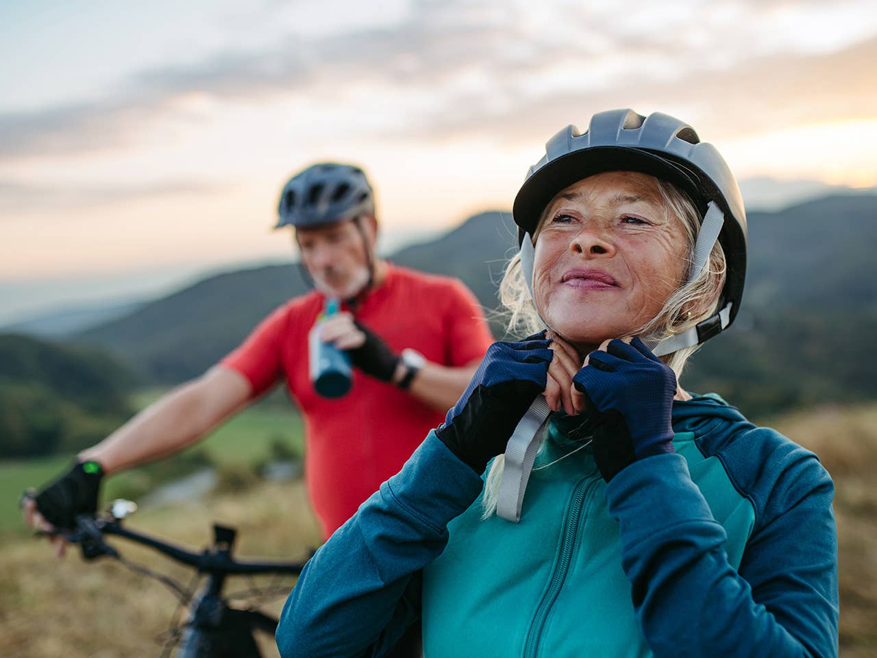 Elderly man and woman buckle bicycle helmets on their heads before starting a bicycle ride in the evening