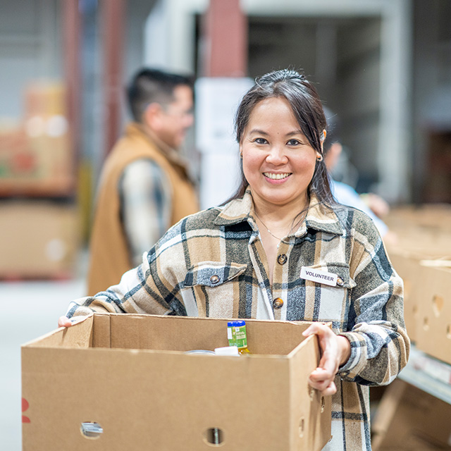 A smiling woman holds a box of food, showcasing her joy and enthusiasm for sharing a meal.
