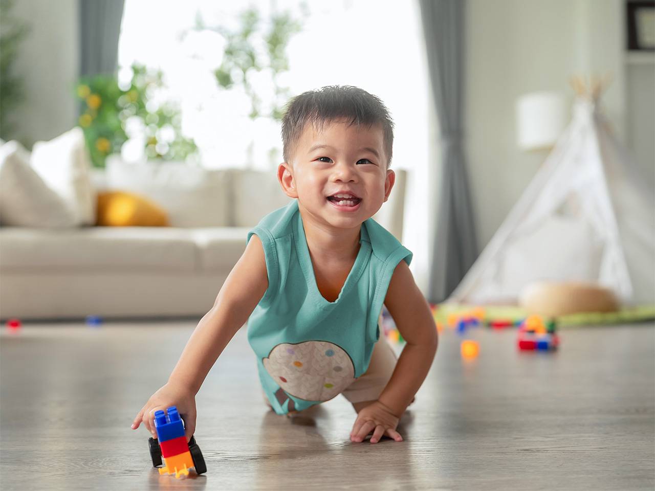 Young Asian boy sits on the floor on his knees while he plays with a plastic block