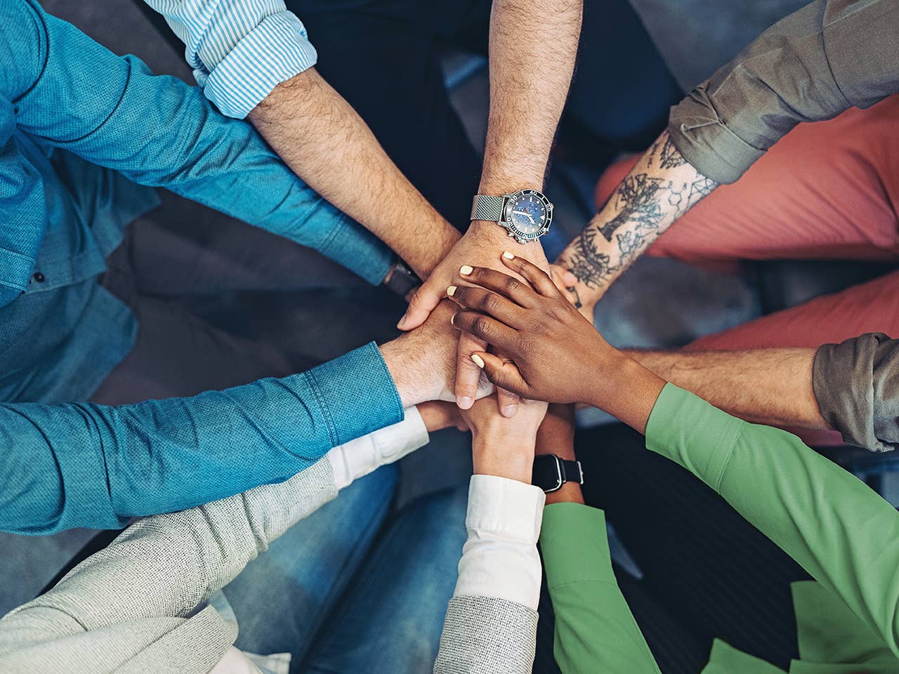 hands of all different skin tones with arms in a circle showing they are working together