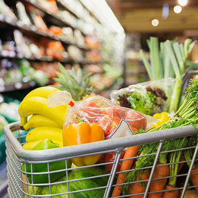 A shopping cart filled with various groceries, including fruits, vegetables, and packaged food items.