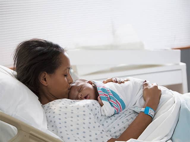 Women laying in a hospital bed while holding her sleeping newborn baby
