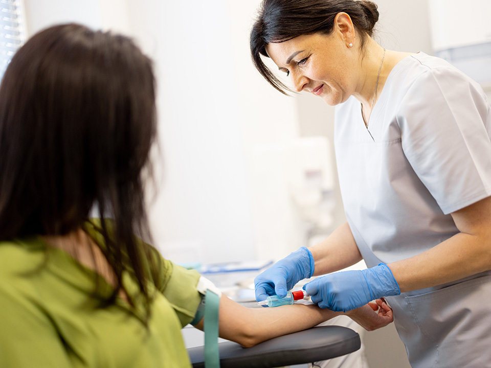 Woman in medical scrubs gently draws blood from a female patient in a Corewell Health lab