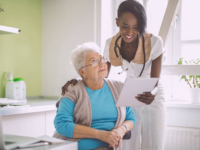 A woman with a stethoscope speaks to an older woman.