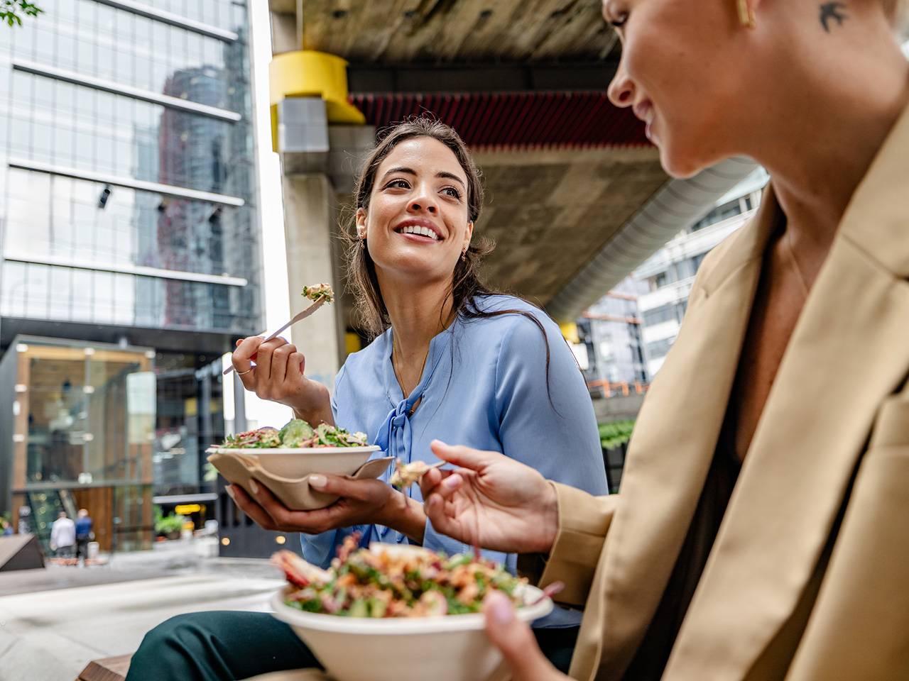 Two people eating fresh salad bowls outdoors in an urban setting, making healthy meal choices on the go.
