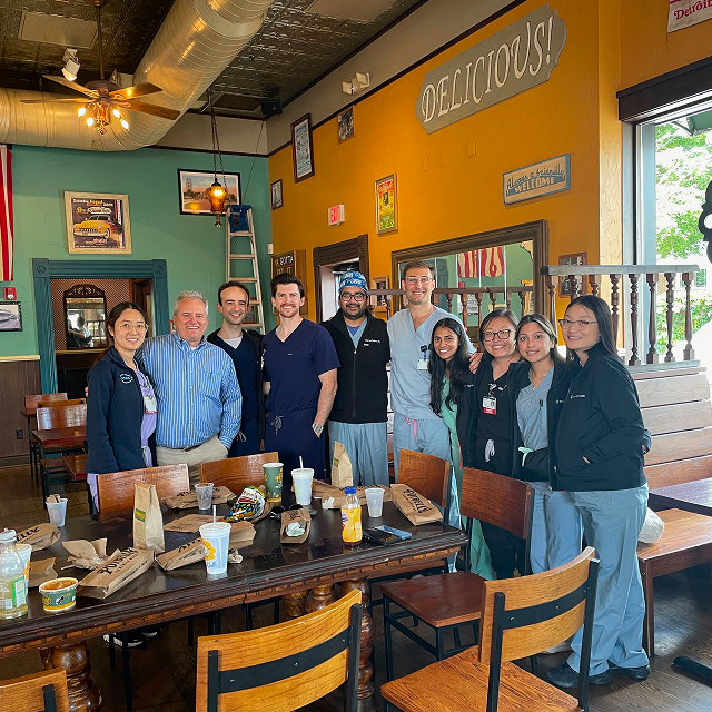 Group of medical trainees and staff standing behind a breakfast table in a restaurant during a community gathering.