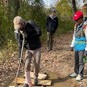Individuals collaborate on a wooden board in a forest, promoting outdoor education and emergency preparedness through WILDS.