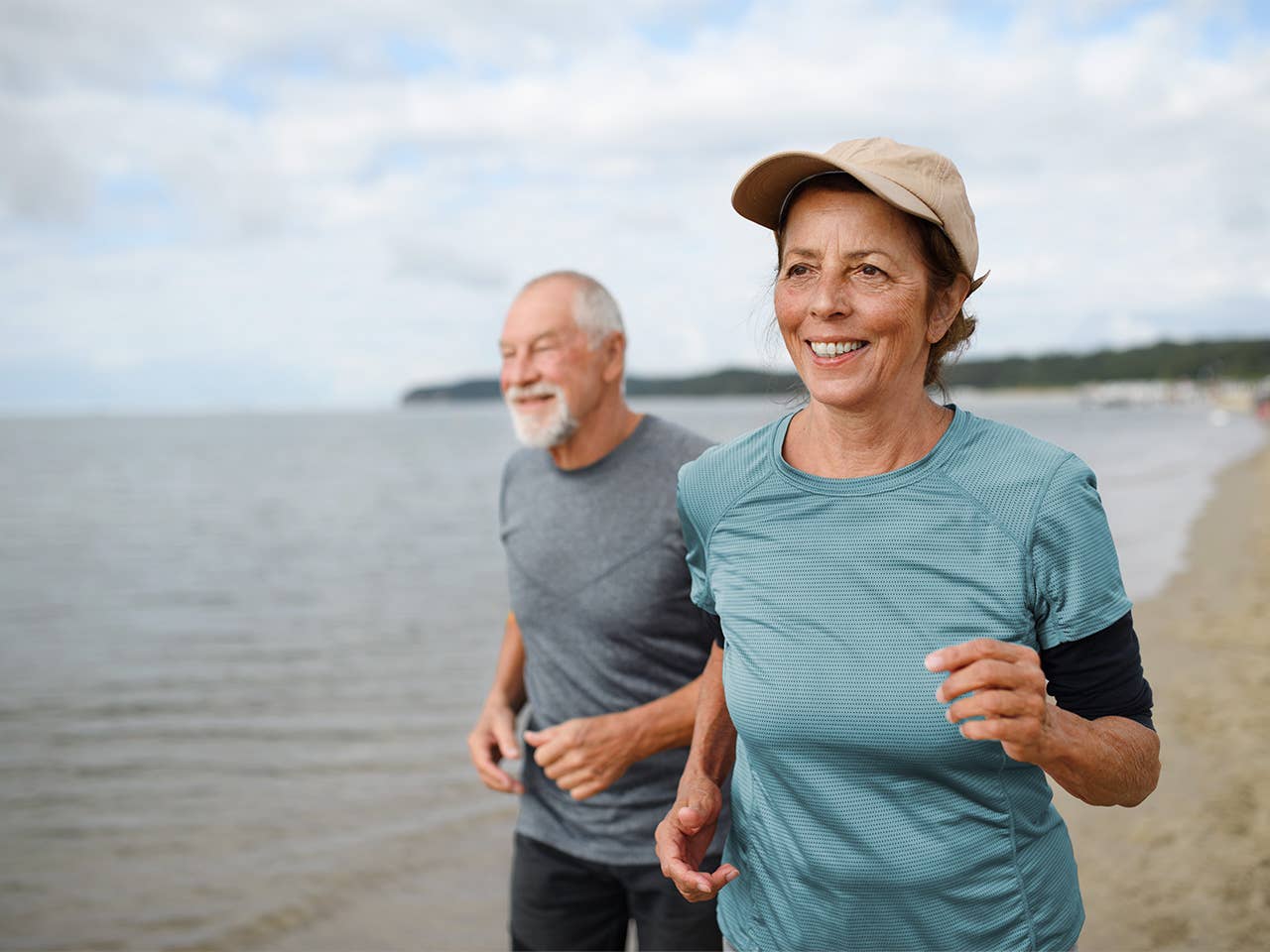 Older man and woman jogging on beach alongside a lake