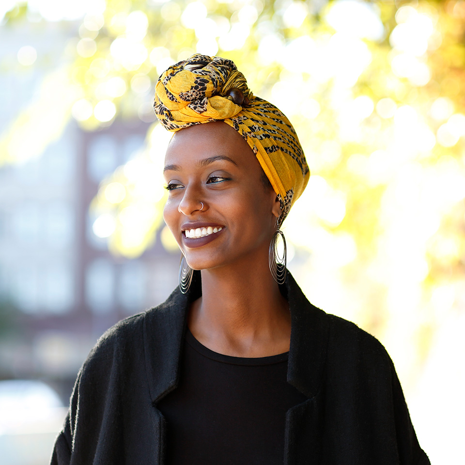 Smiling young Black woman with a yellow head wrap stands in the sunshine