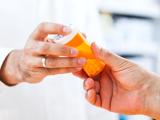 A person passing a prescription bottle to another individual in a healthcare setting.