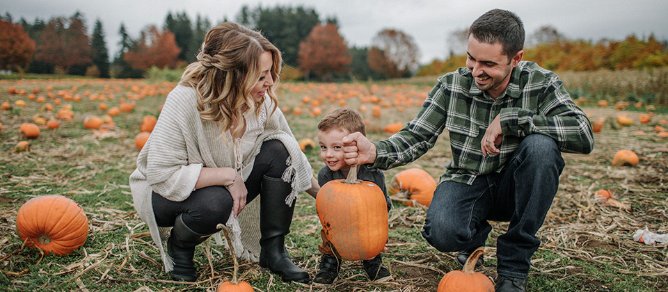 A family enjoying a day at a pumpkin patch, surrounded by pumpkins and vibrant autumn foliage.