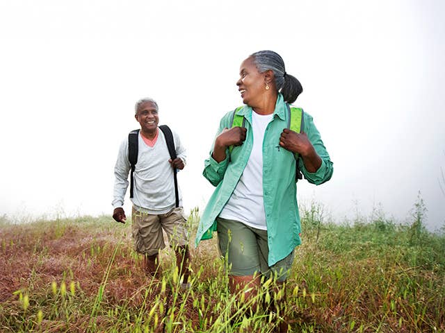 Older Black man and woman hike together through a field