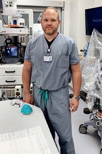 Dr. Chris Hutchinson, an EM Faculty Mentor, stands in scrubs before a hospital room, ready to assist patients.