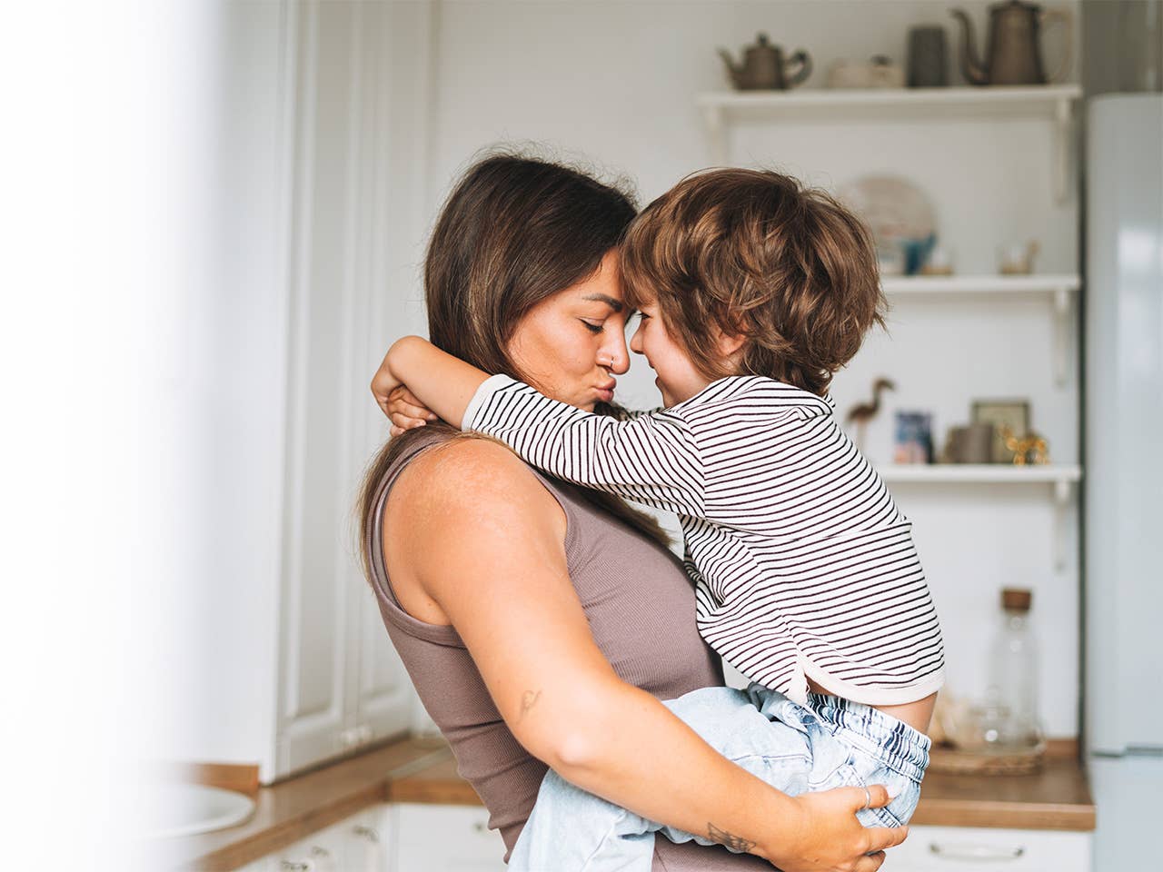 Woman lifts up and hugs a young boy as they touch foreheads