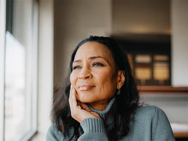 A woman gazes thoughtfully out of a window, her expression reflecting anxiety and depression.