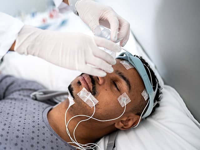 A male patient in the hospital going through a sleep study is getting sensors placed on his head and face
