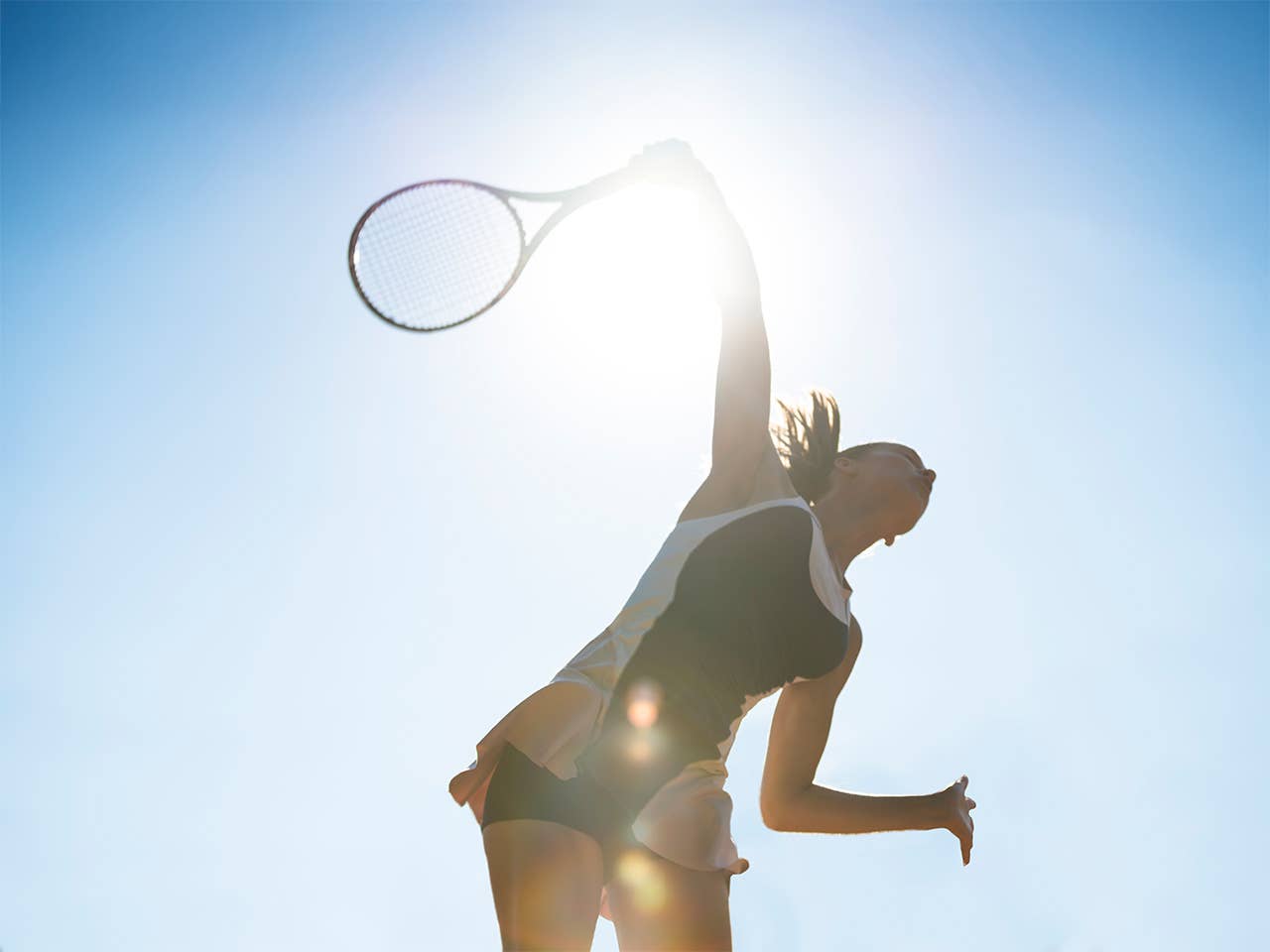 Woman swings a tennis racket in the bright sunshine