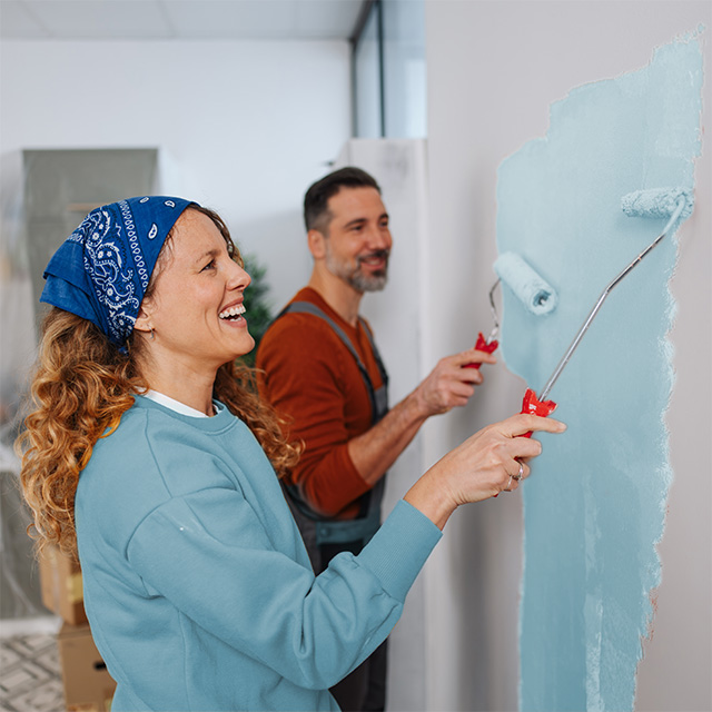 A man and woman painting a wall together with blue paint, focused on their task and enjoying the activity.