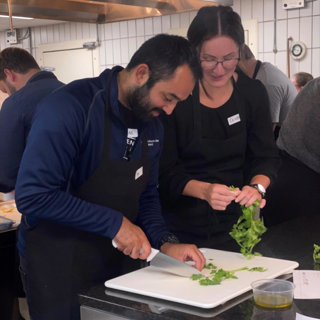 chef cutting up herbs while another chef is watching