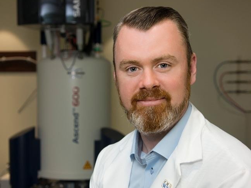 Stewart Graham, PhD, a white man with brown hair and a beard, wearing a white lab coat