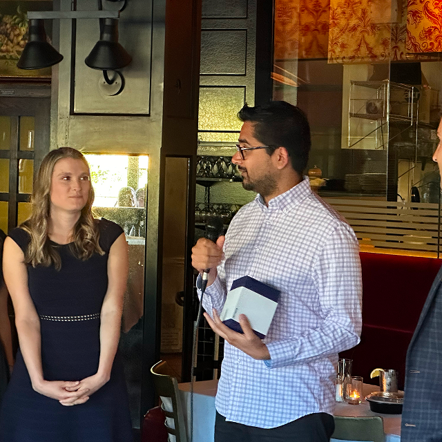Person speaking into a microphone while presenting an award to another person at a restaurant gathering
