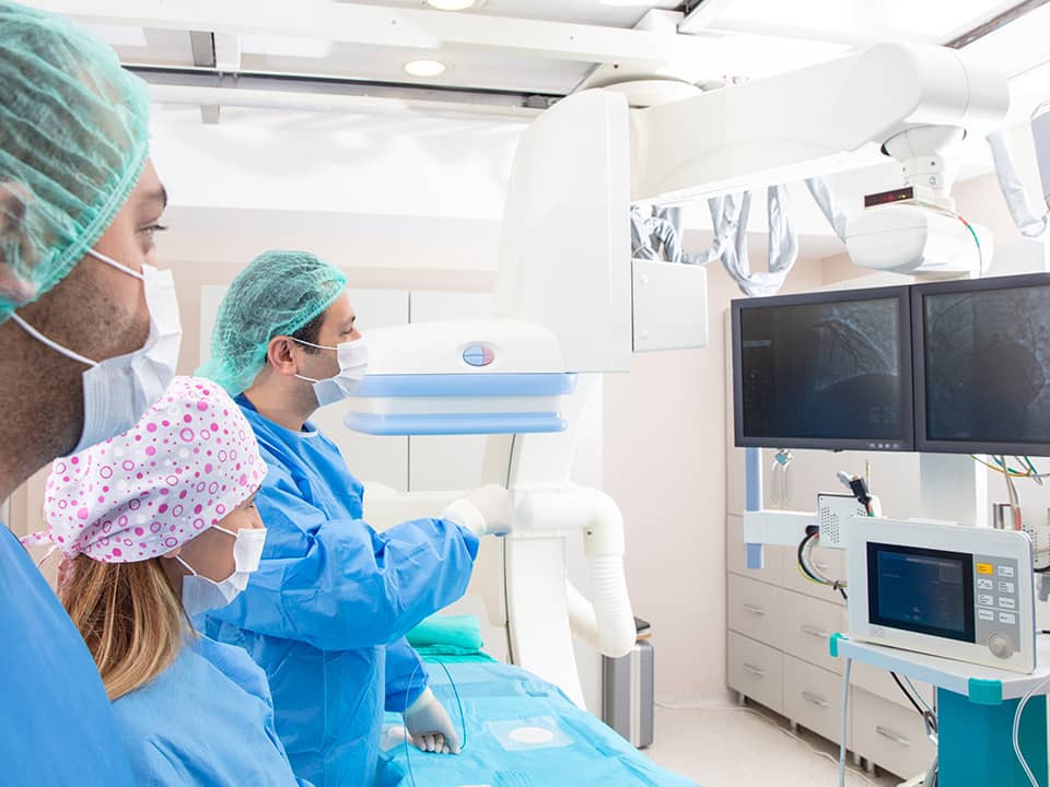 Medical team in a cardiac catheterization lab viewing imaging monitors during an interventional cardiology procedure.