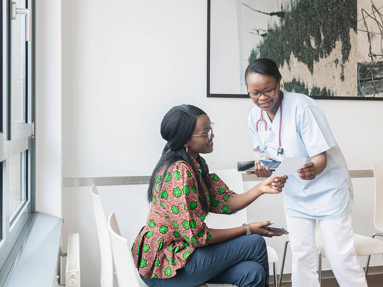 A woman in a hospital room converses with another woman, both appearing engaged and supportive.