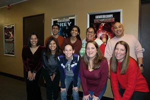 People gathered together, smiling for a photo in front of a movie poster promoting Wilderness Medicine activities.