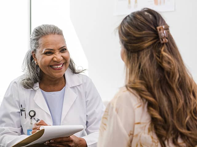 A smiling Corewell Health employer services team member sits across from a female patient as she takes notes on a clipboard