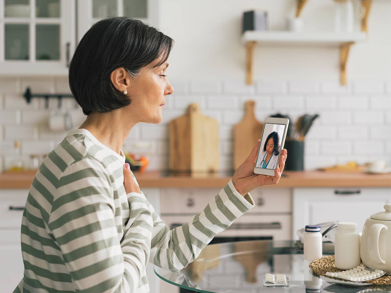 Woman in a white and green striped sweater holds up her phone while on a virtual visit with a provider