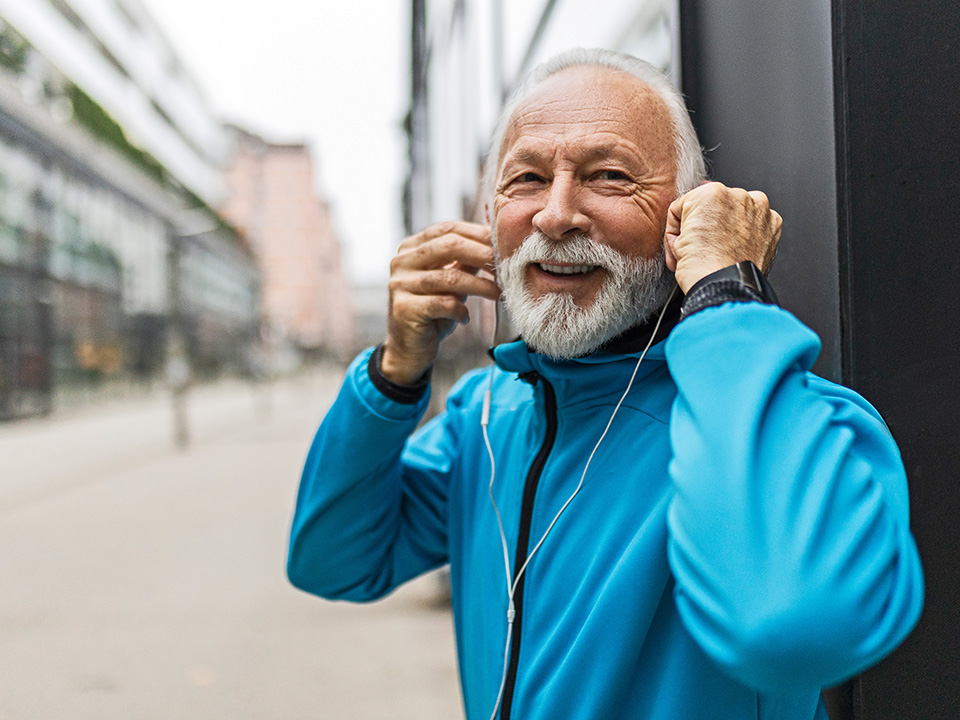 A bearded older man wearing earphones, appearing engaged in audio content.