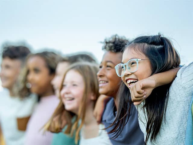Group of six smiling boys and girls standing side-by-side outdoors