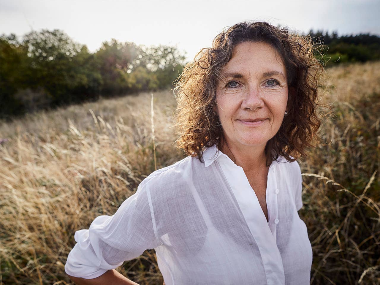 Older white woman stands in a field of wild grasses in the evening sun