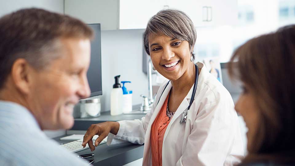 Smiling Corewell Health genetic counselor speaks with a man and woman in an exam room