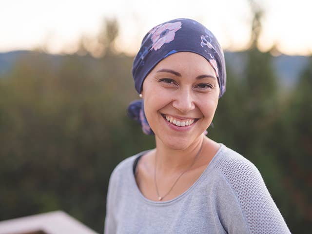 Smiling young white woman wearing a purple bandana on her head stands outdoors in the evening sunlight