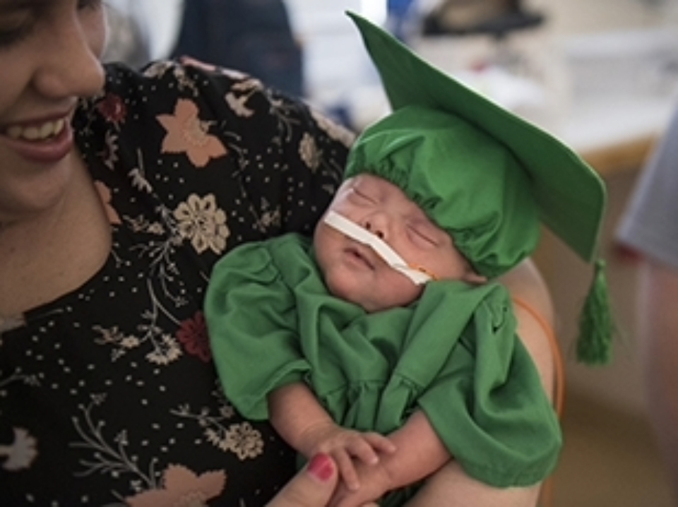 Small baby in a green graduate cap after being discharged from the small baby unit