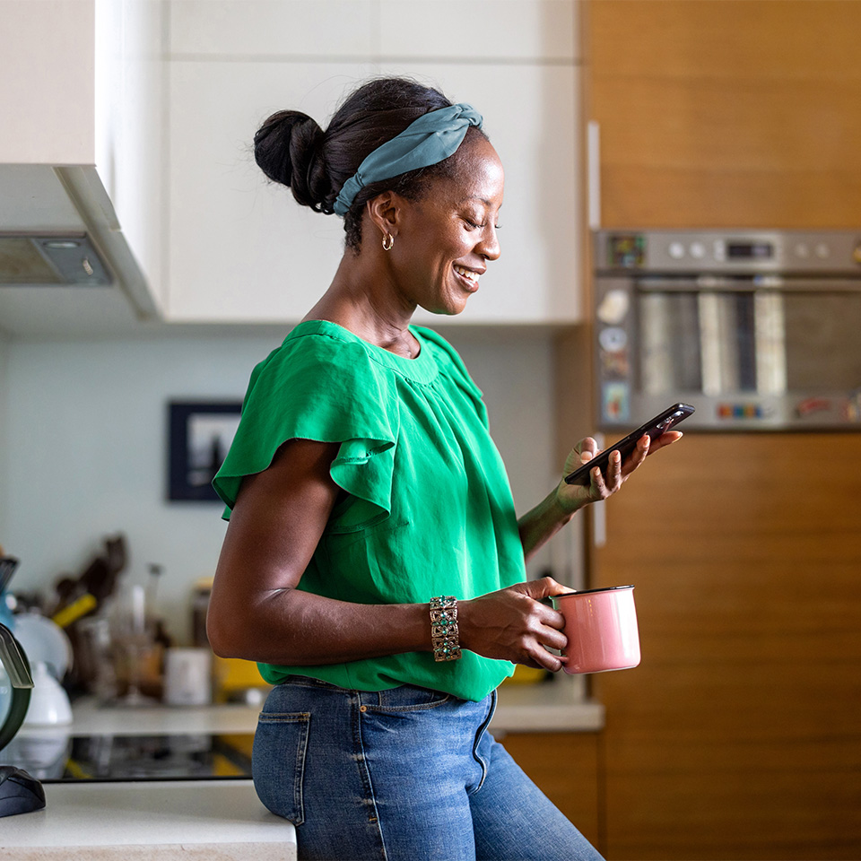 Black woman in a green shirt smiles while looking at phone