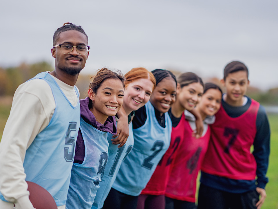 Group of teenage girls on a soccer team stand side-by-side with their coach, smiling
