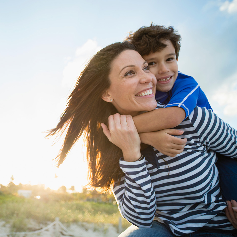 A woman and a child smile together on a sunny beach, enjoying their time by the ocean.