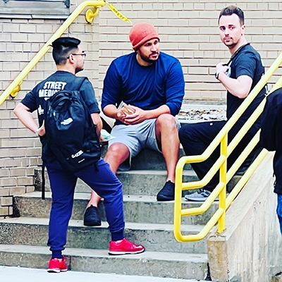 A group of men seated on building steps, engaged in conversation, reflecting community involvement and support initiatives.