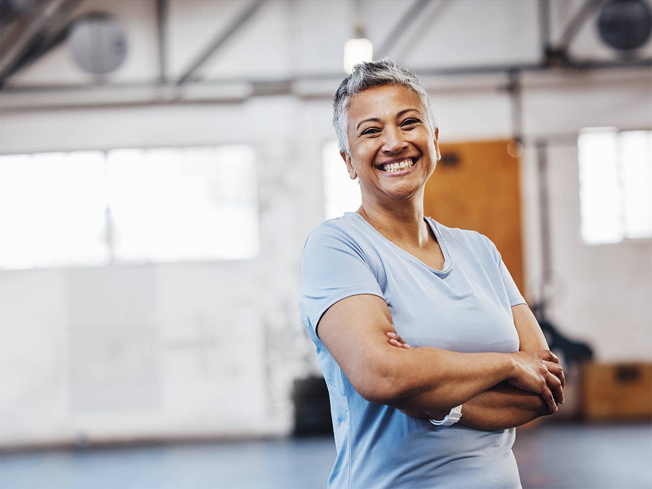 Smiling middle aged woman with short hair crosses her arms while standing in a gym
