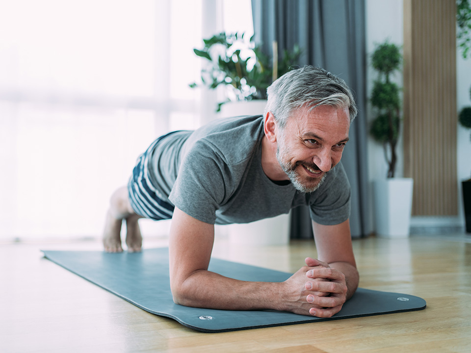 Man with grey hair and beard does a plank on a yoga mat