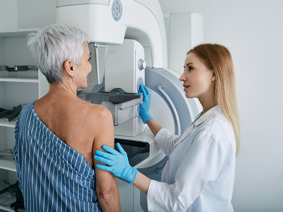 Corewell Health breast care specialist helps an older woman patient prepare for a mammogram