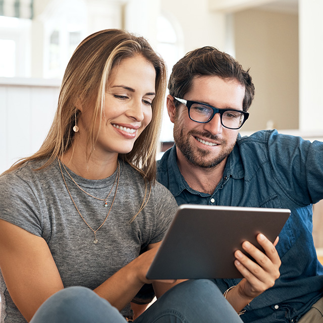 Smiling young man and young woman sit next to each other and look at a tablet together