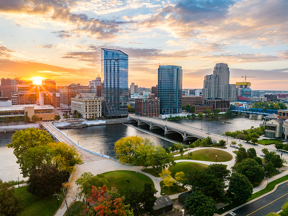 Grand Rapids Michigan city skyline in autumn, featuring vibrant trees with colorful foliage against a backdrop of tall buildings.