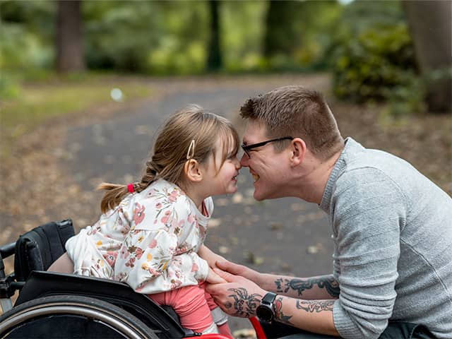 Smiling Black girl with curly brown hair holds on to her mother's back as she is carried in a park outdoors
