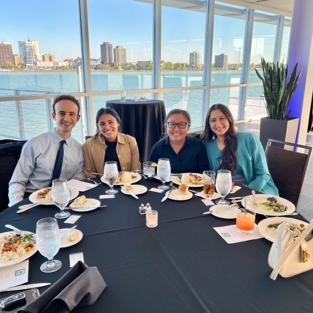 Group of residents in front of a glass window overlooking water and a city skyline eating a meal and posing for a group photo