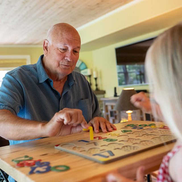A man and a young girl joyfully playing a board game together on a table, surrounded by colorful game pieces.