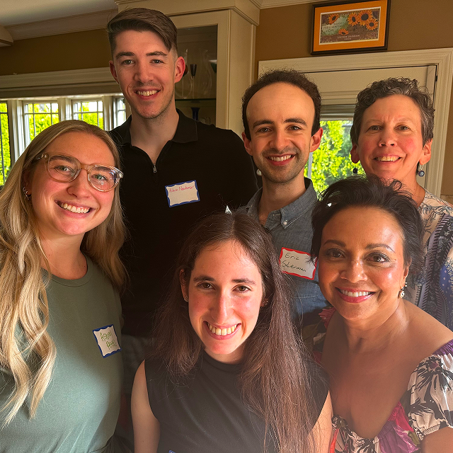 Six attendees pose together indoors at a community gathering, standing and seated in a small group.
